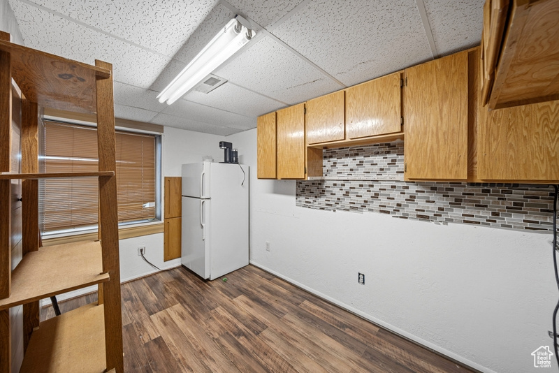 Kitchen with freestanding refrigerator, backsplash, a paneled ceiling, dark wood-style floors, and baseboards