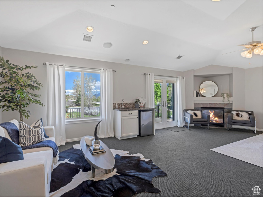Living area featuring dark carpet, a glass covered fireplace, vaulted ceiling, baseboards, and a ceiling fan