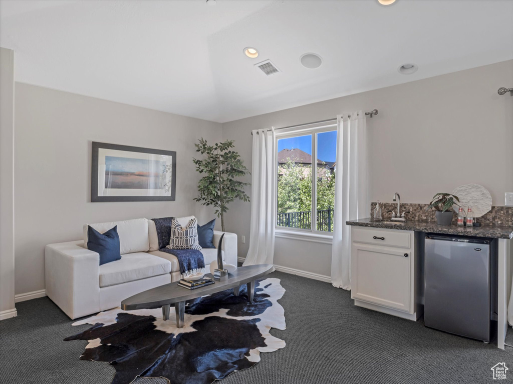Living room featuring dark colored carpet, bar with sink, and baseboards