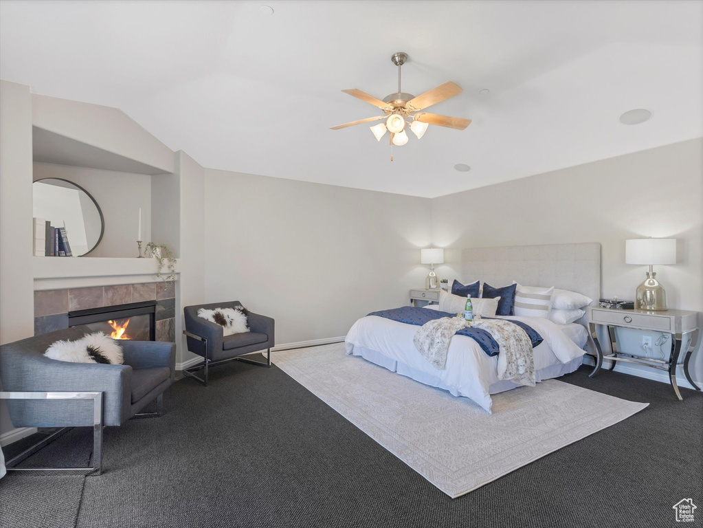 Carpeted bedroom featuring a tile fireplace, vaulted ceiling, ceiling fan, and baseboards