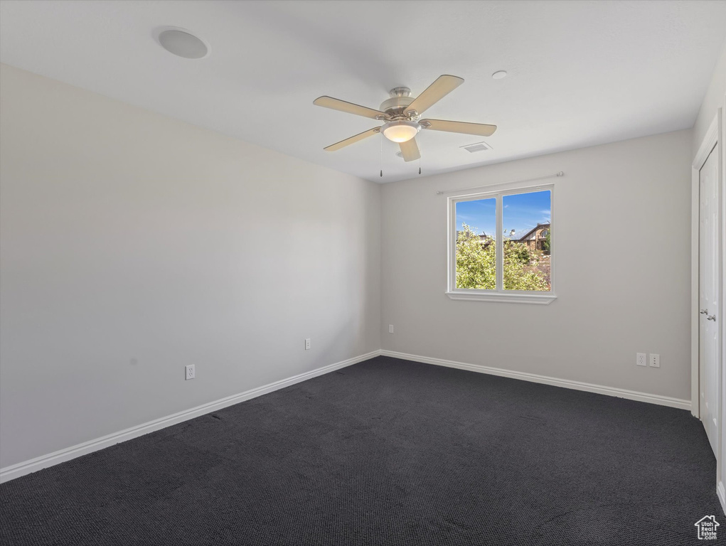 Spare room with a ceiling fan, dark carpet, and baseboards