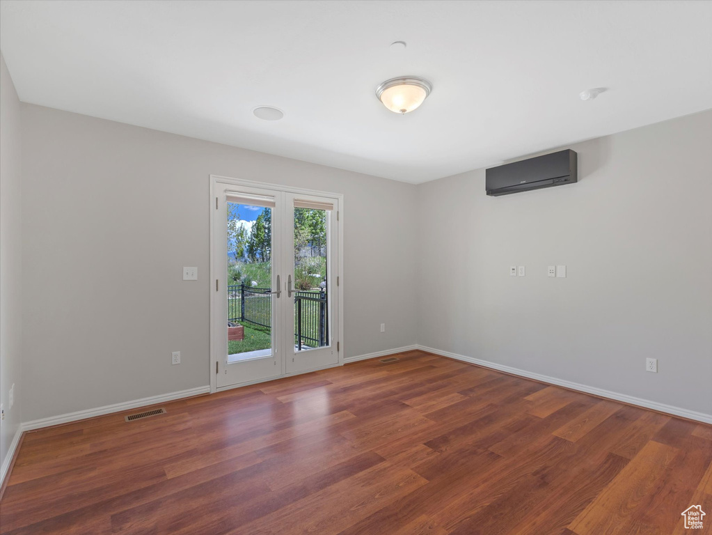 Unfurnished room with a wall mounted AC, wood finished floors, baseboards, and french doors
