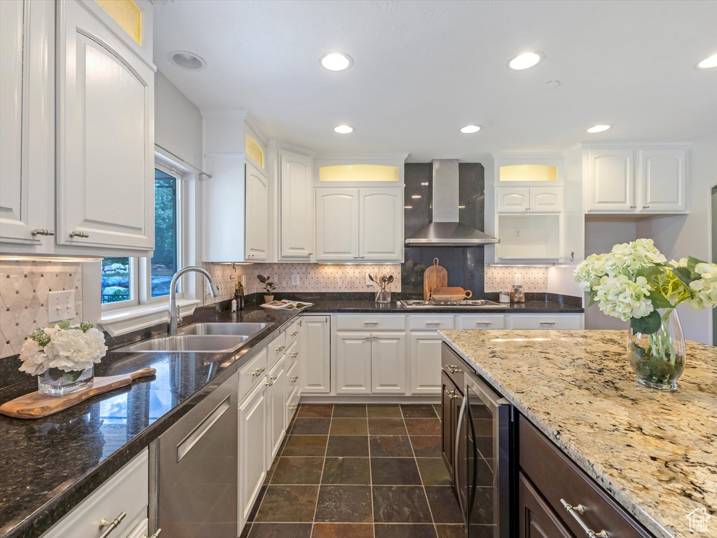 Kitchen with wall chimney exhaust hood, a sink, stainless steel dishwasher, wine cooler, and white cabinets