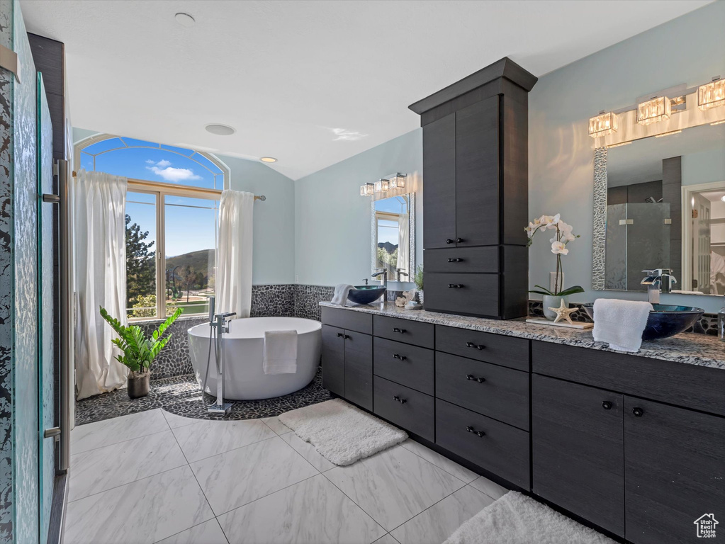Full bathroom featuring healthy amount of natural light, a soaking tub, double vanity, vaulted ceiling, and a shower stall