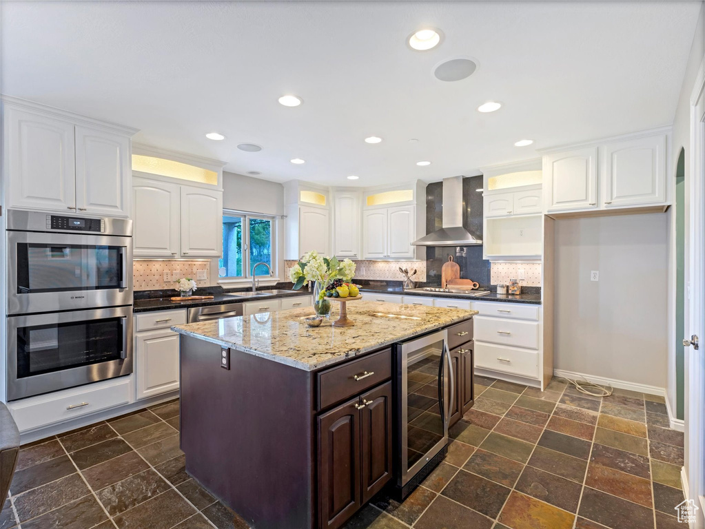 Kitchen with beverage cooler, wall chimney range hood, appliances with stainless steel finishes, decorative backsplash, and recessed lighting