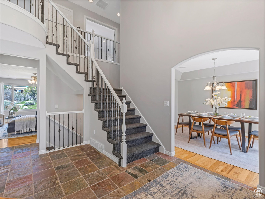 Staircase featuring stone tile flooring, baseboards, arched walkways, a chandelier, and a high ceiling