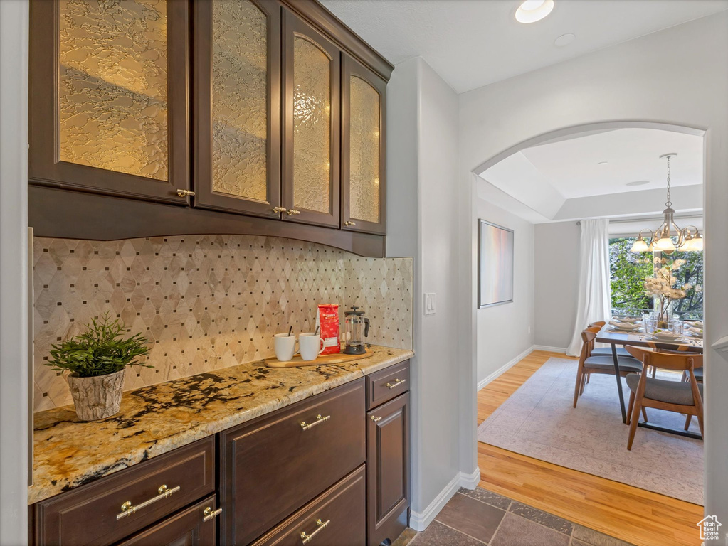 Indoor dry bar featuring arched walkways, tasteful backsplash, baseboards, a chandelier, and pendant lighting