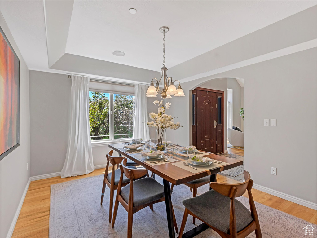 Dining room with arched walkways, light wood finished floors, a chandelier, and baseboards