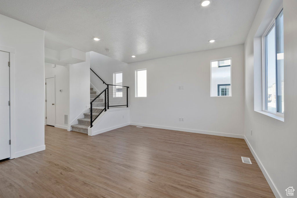 Unfurnished living room featuring light wood-style floors, stairway, healthy amount of natural light, baseboards, and recessed lighting