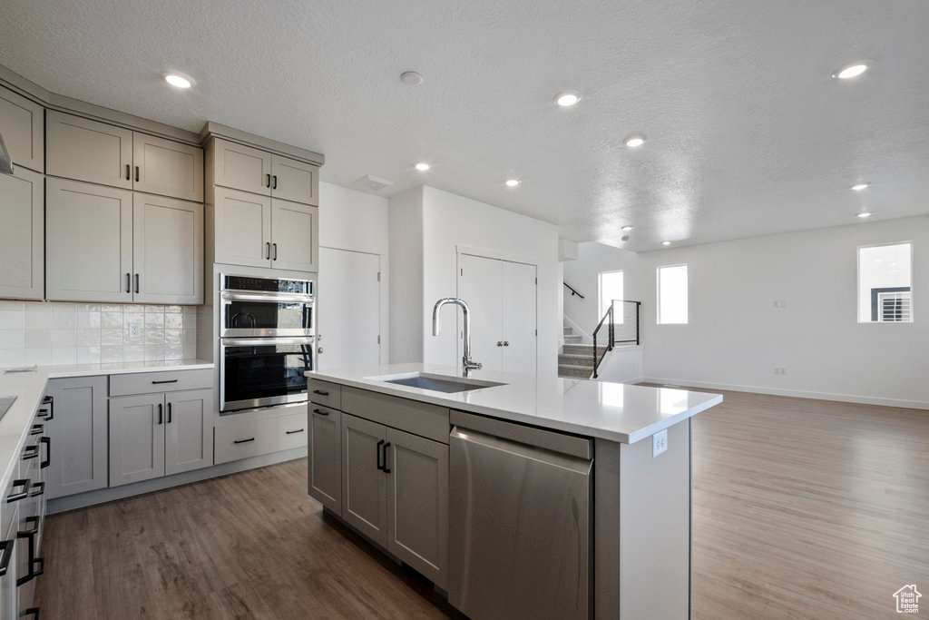 Kitchen with appliances with stainless steel finishes, a sink, gray cabinetry, wood finished floors, and recessed lighting