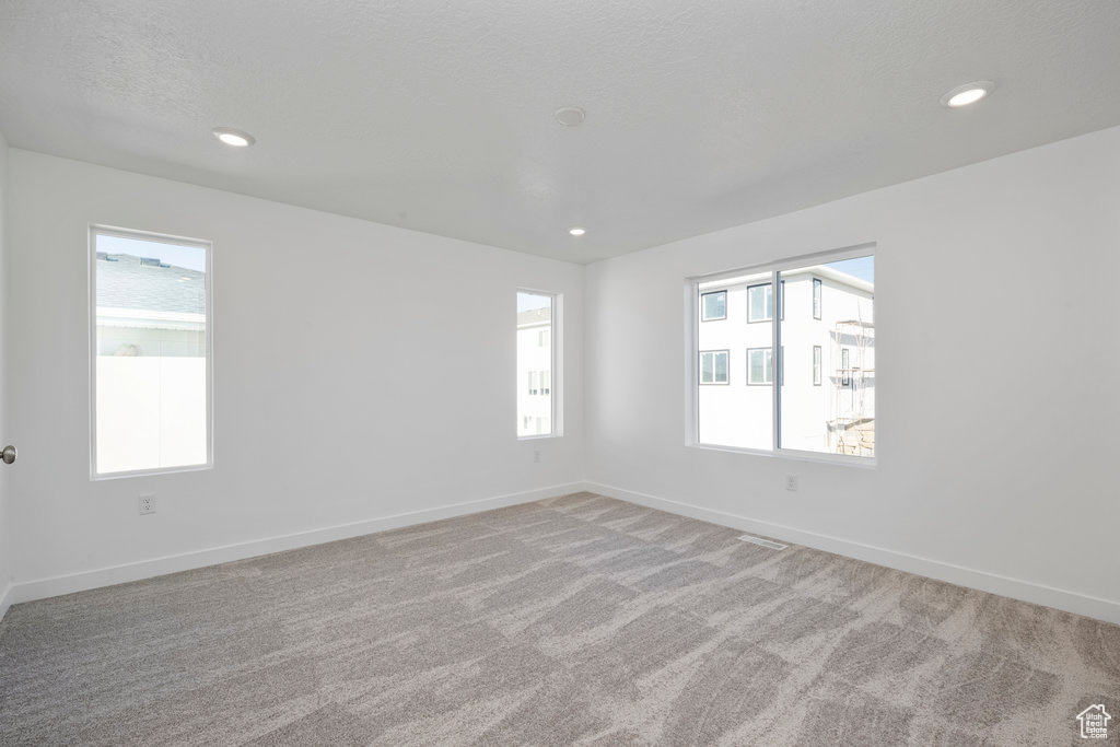 Empty room featuring light carpet, baseboards, recessed lighting, and a textured ceiling