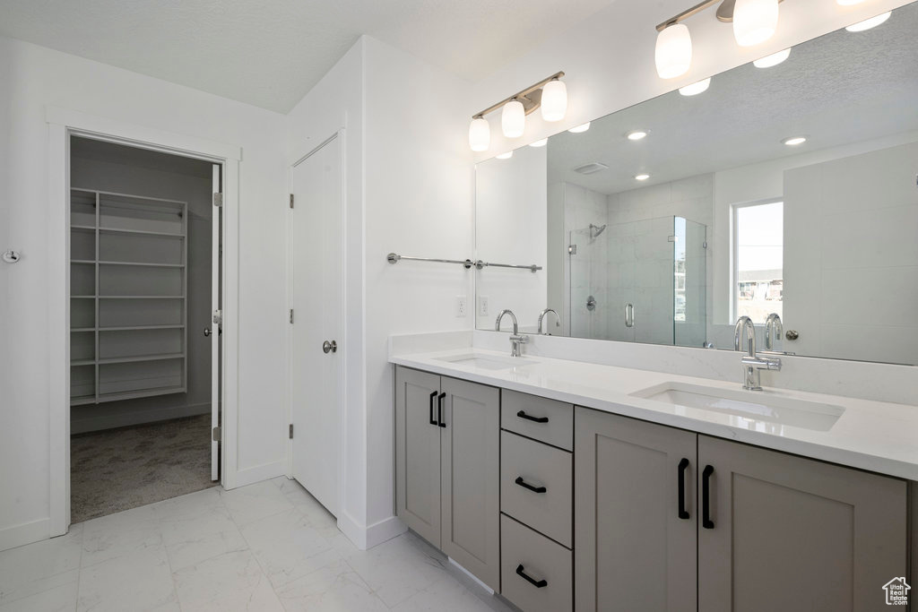 Full bathroom with a stall shower, marble look tiles, a spacious closet, double vanity, and baseboards