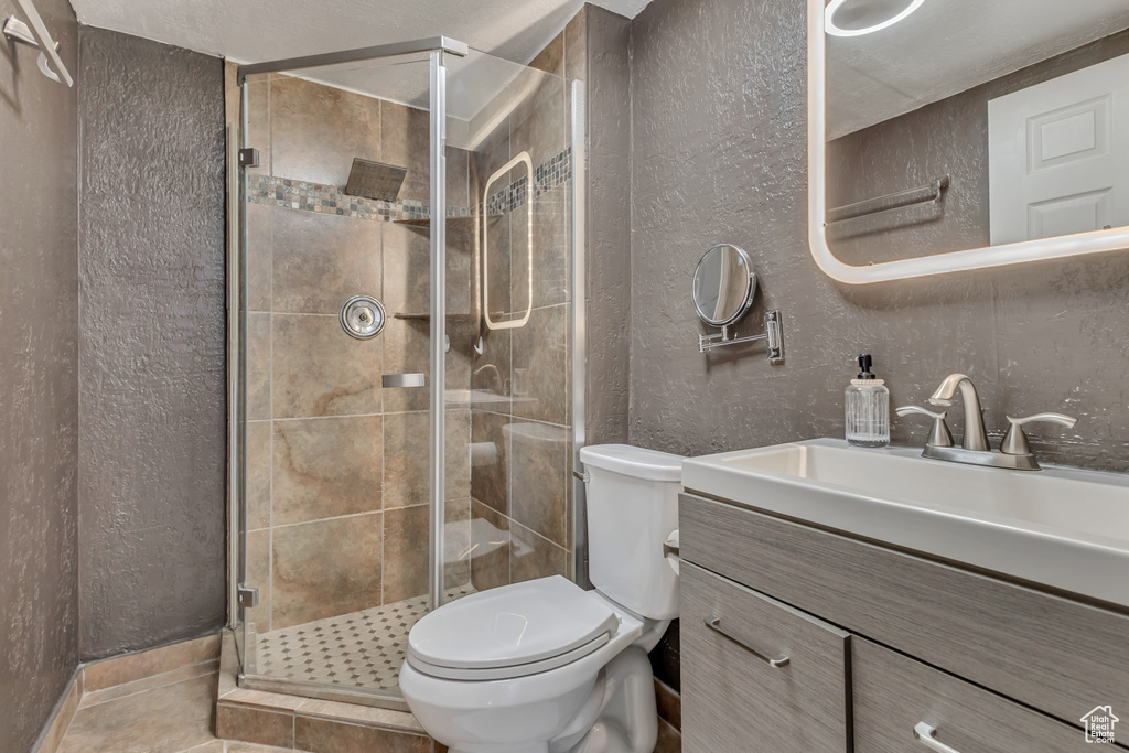 Full bath with a textured wall, toilet, a stall shower, vanity, and tile patterned flooring