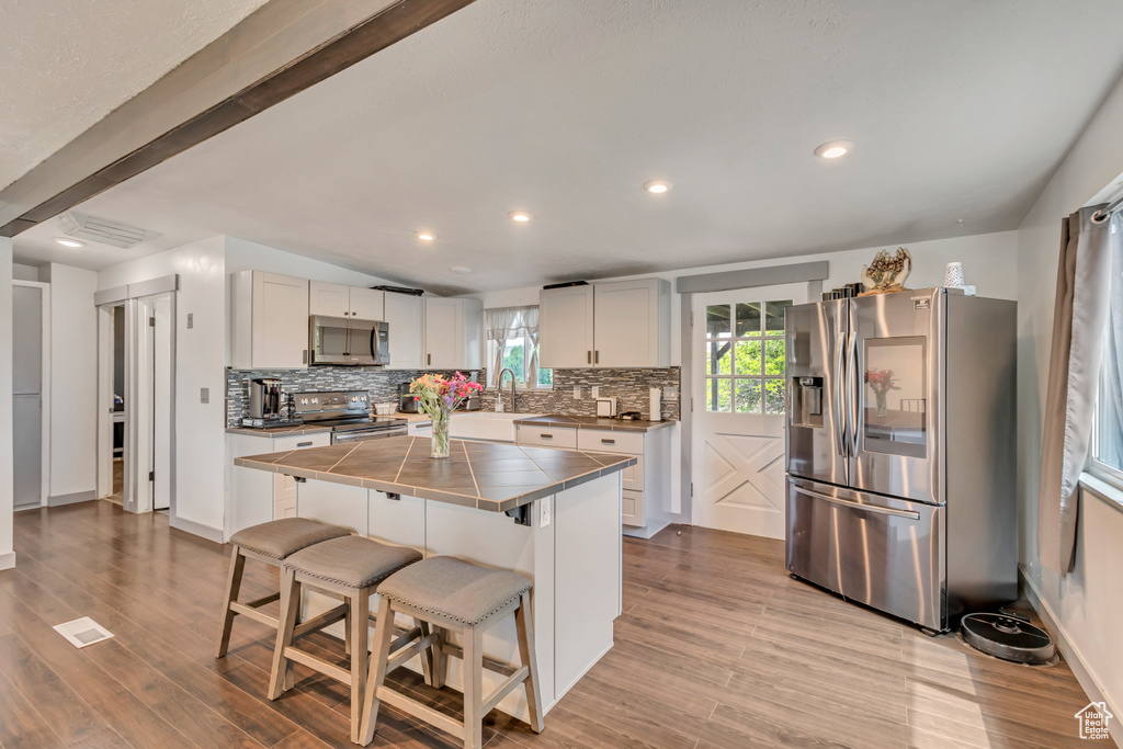 Kitchen with stainless steel appliances, tile countertops, tasteful backsplash, a breakfast bar area, and wood finished floors