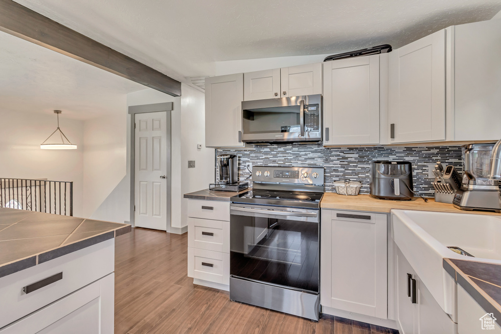 Kitchen with appliances with stainless steel finishes, decorative backsplash, light wood-type flooring, white cabinets, and beamed ceiling