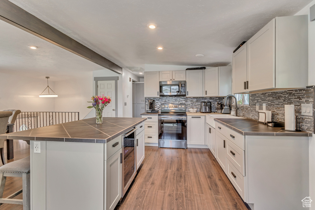 Kitchen featuring appliances with stainless steel finishes, a sink, decorative backsplash, a breakfast bar, and light wood-type flooring