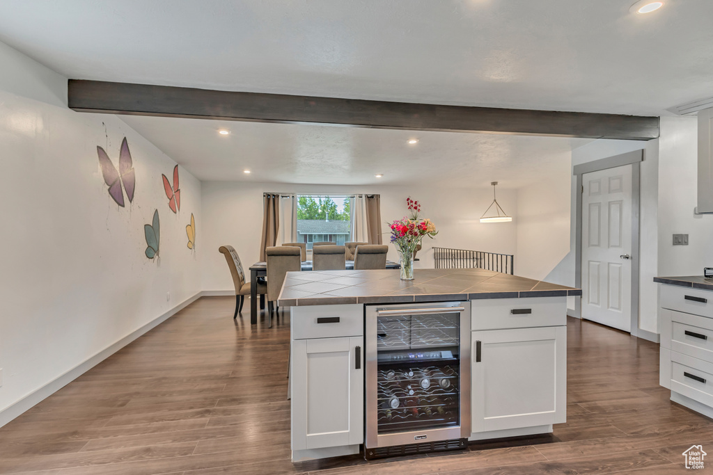 Kitchen with beverage cooler, tile counters, white cabinets, beam ceiling, and wood finished floors