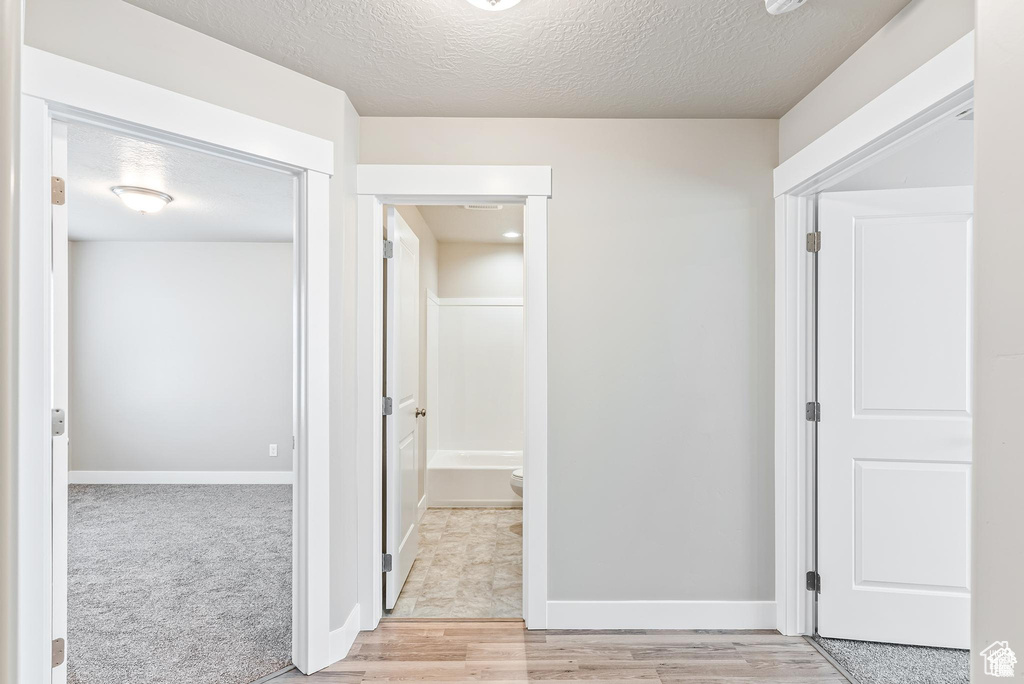 Corridor featuring a textured ceiling, baseboards, and light wood-type flooring