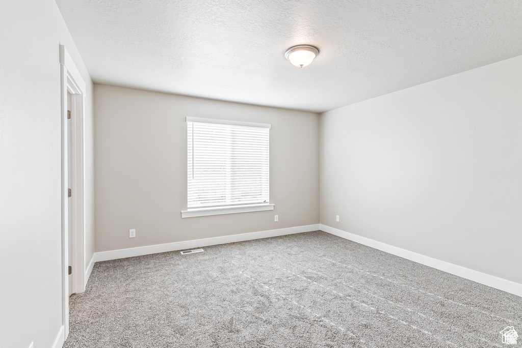 Carpeted spare room featuring a textured ceiling and baseboards