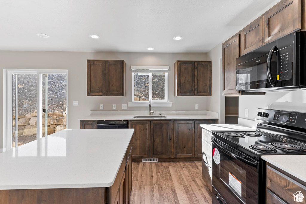 Kitchen with black appliances, a sink, light countertops, light wood-style floors, and recessed lighting