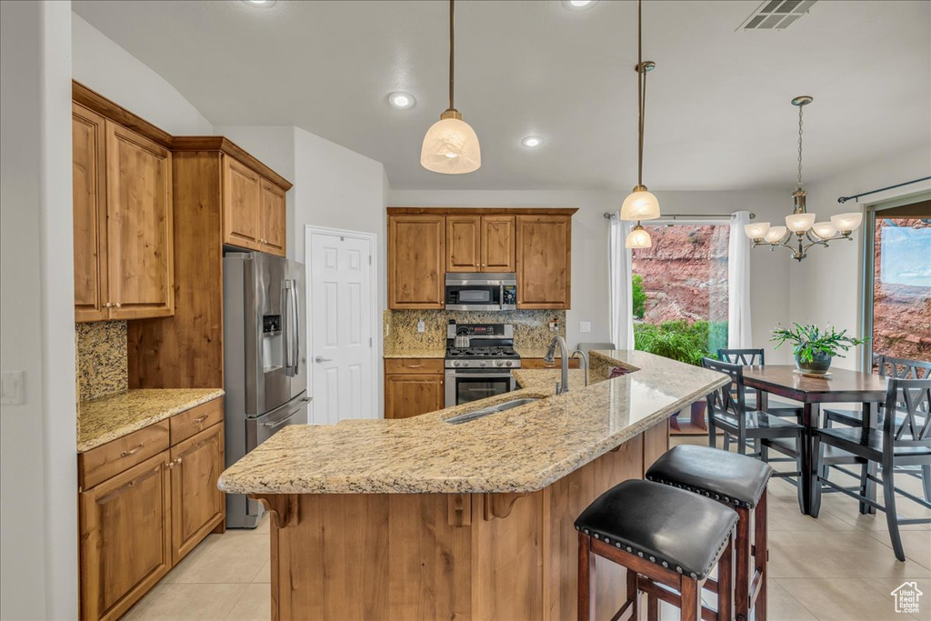 Kitchen with appliances with stainless steel finishes, a sink, light tile patterned floors, brown cabinets, and decorative backsplash
