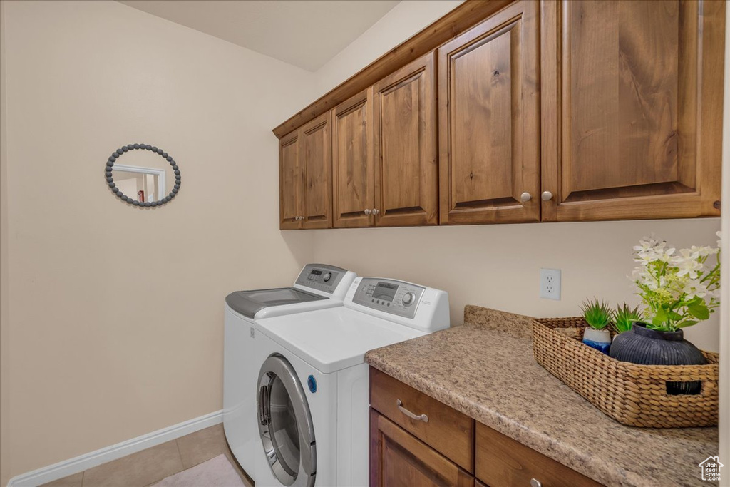 Laundry room with cabinet space, washer and dryer, baseboards, and light tile patterned floors