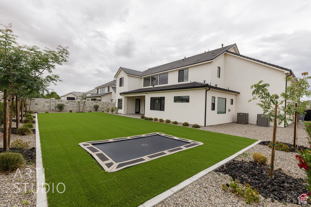 Rear view of property featuring a trampoline, central AC unit, stucco siding, and a patio