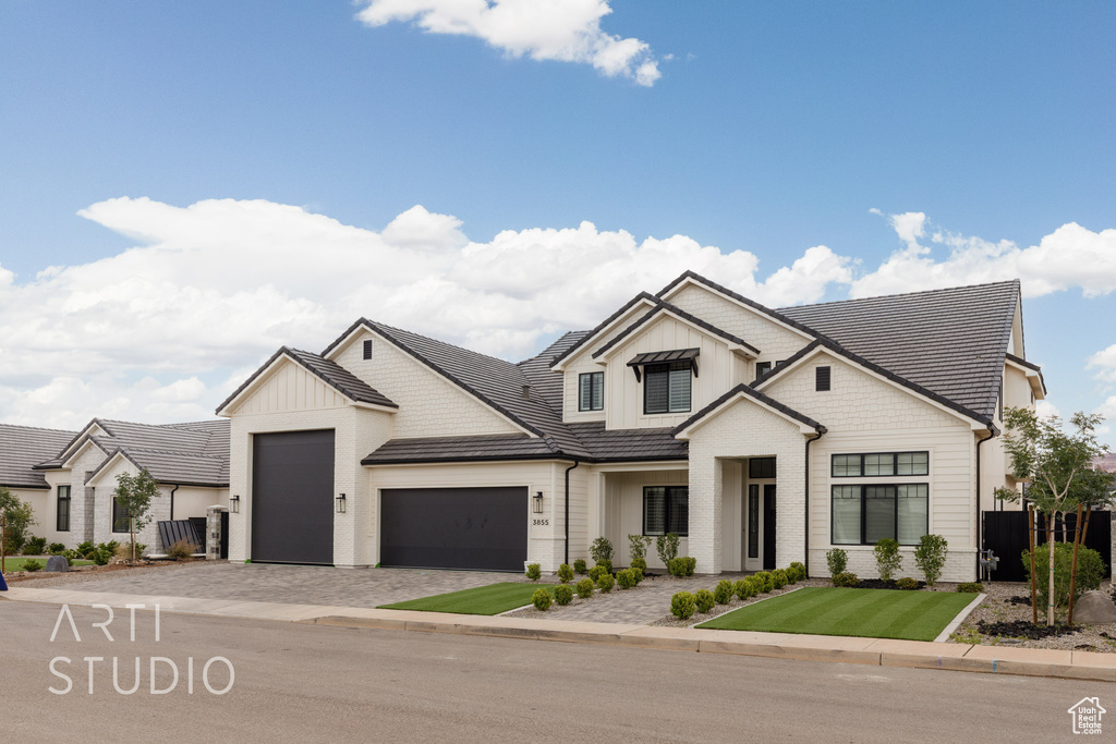 Modern farmhouse featuring an attached garage, board and batten siding, decorative driveway, and fence