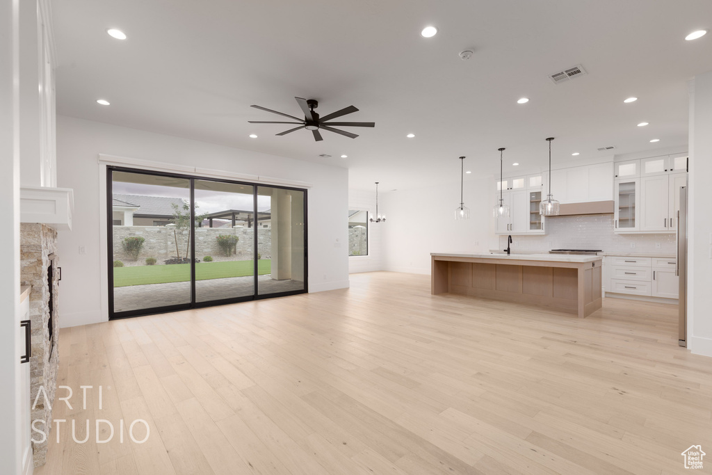 Unfurnished living room featuring a ceiling fan, light wood-style floors, recessed lighting, a stone fireplace, and a sink