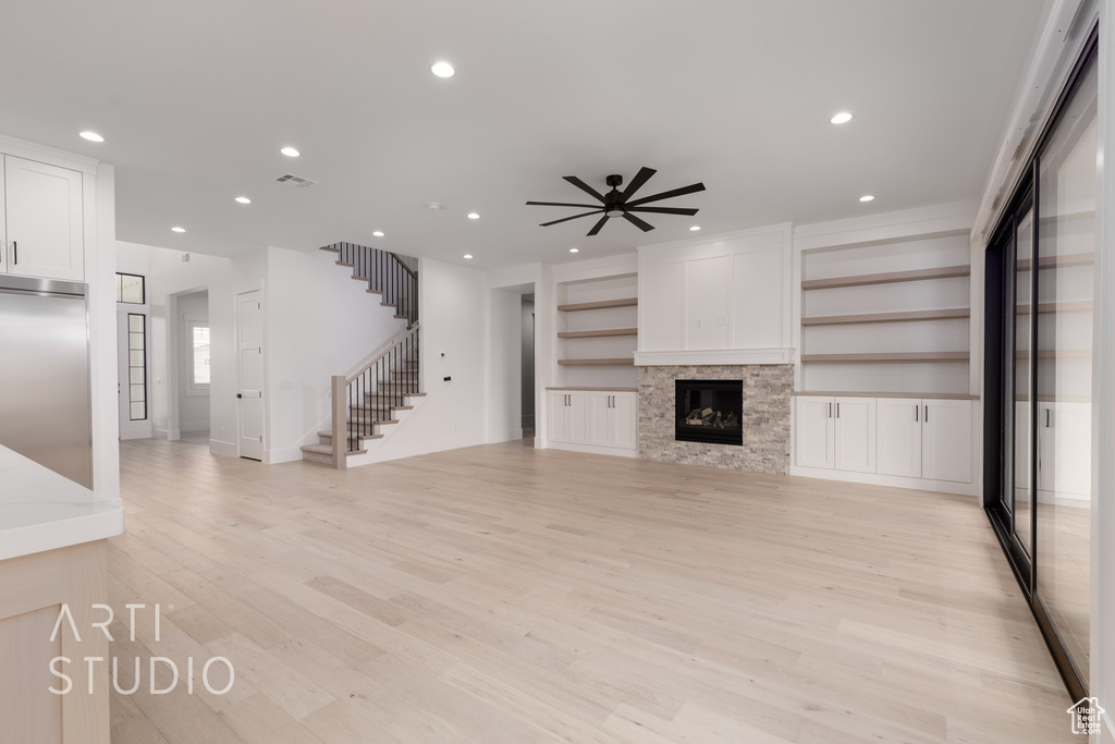 Unfurnished living room featuring stairs, a ceiling fan, recessed lighting, light wood-type flooring, and a glass covered fireplace