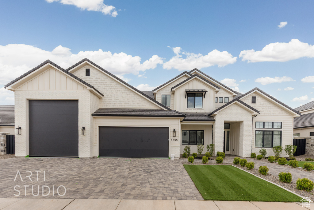 Modern farmhouse with board and batten siding, a garage, decorative driveway, brick siding, and a front lawn