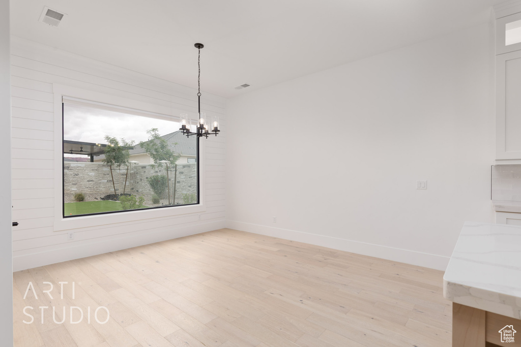 Unfurnished dining area with a chandelier, light wood finished floors, and baseboards