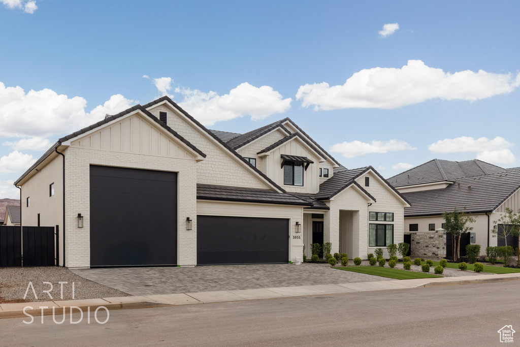 Modern inspired farmhouse featuring a garage, board and batten siding, decorative driveway, brick siding, and fence