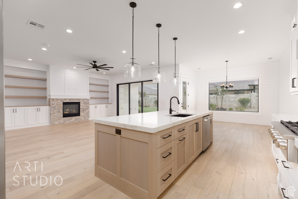 Kitchen featuring a sink, light wood-style floors, dishwasher, a stone fireplace, and recessed lighting
