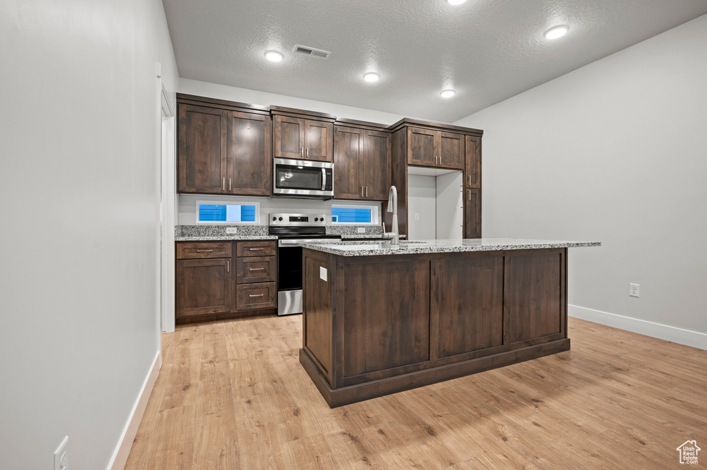 Kitchen with stainless steel appliances, a sink, baseboards, dark brown cabinetry, and light wood-style floors