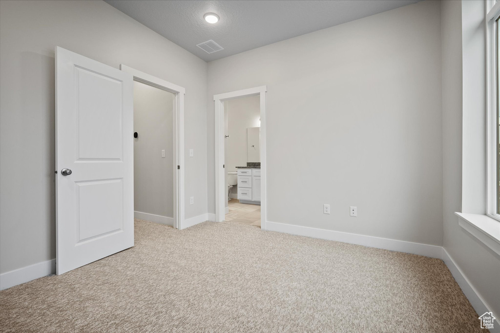 Unfurnished bedroom with light colored carpet, baseboards, and ensuite bath