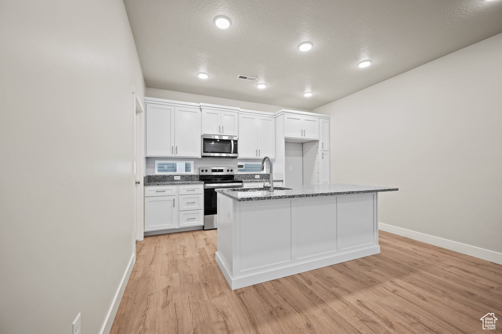 Kitchen featuring stainless steel appliances, baseboards, light wood-type flooring, white cabinetry, and dark stone counters
