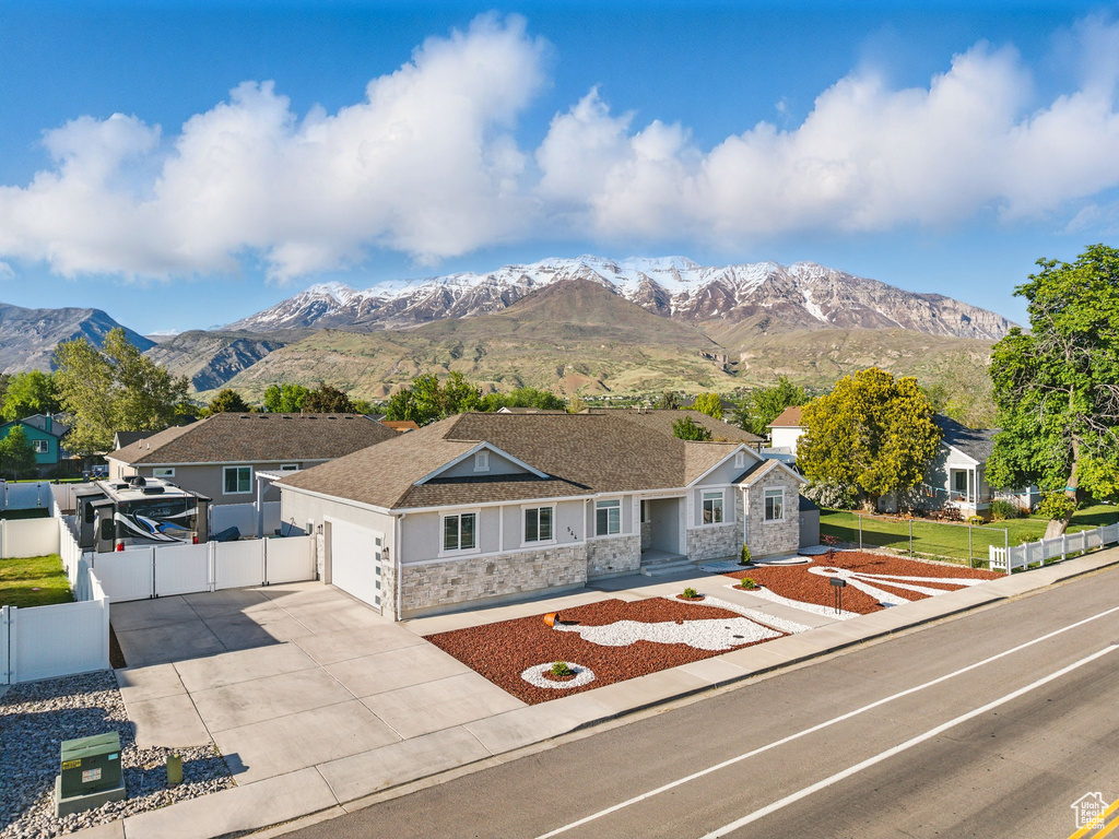 Ranch-style home featuring stone siding, an attached garage, concrete driveway, fence, and a mountain view