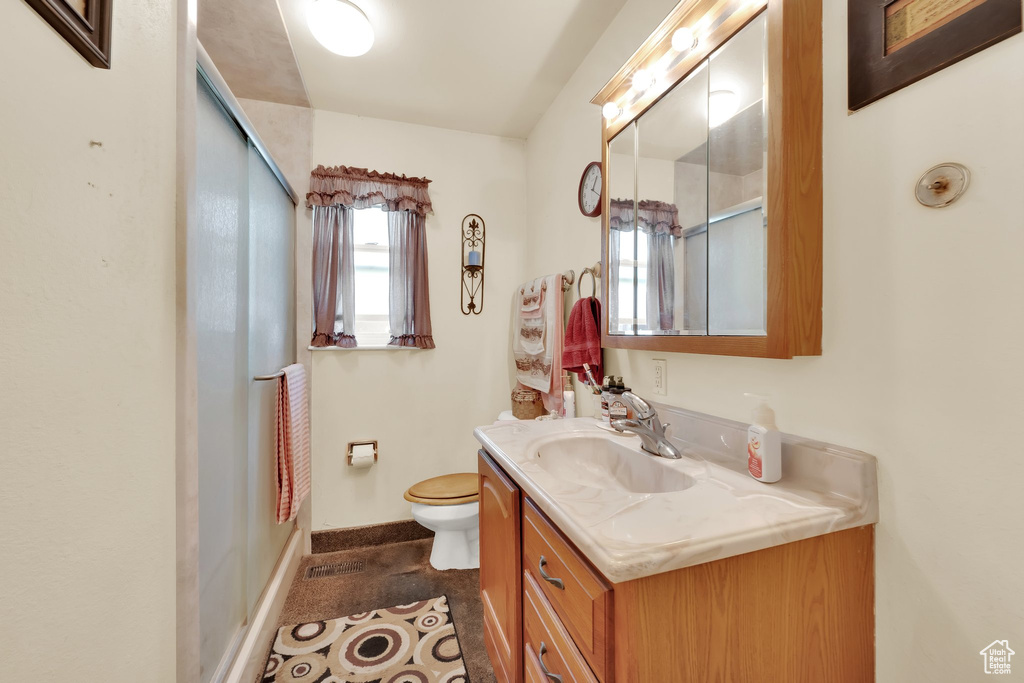 Full bath featuring vanity, toilet, a shower with door, and baseboards