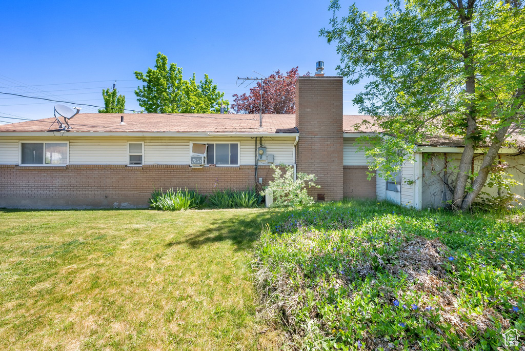 Rear view of house with brick siding, a chimney, and a yard