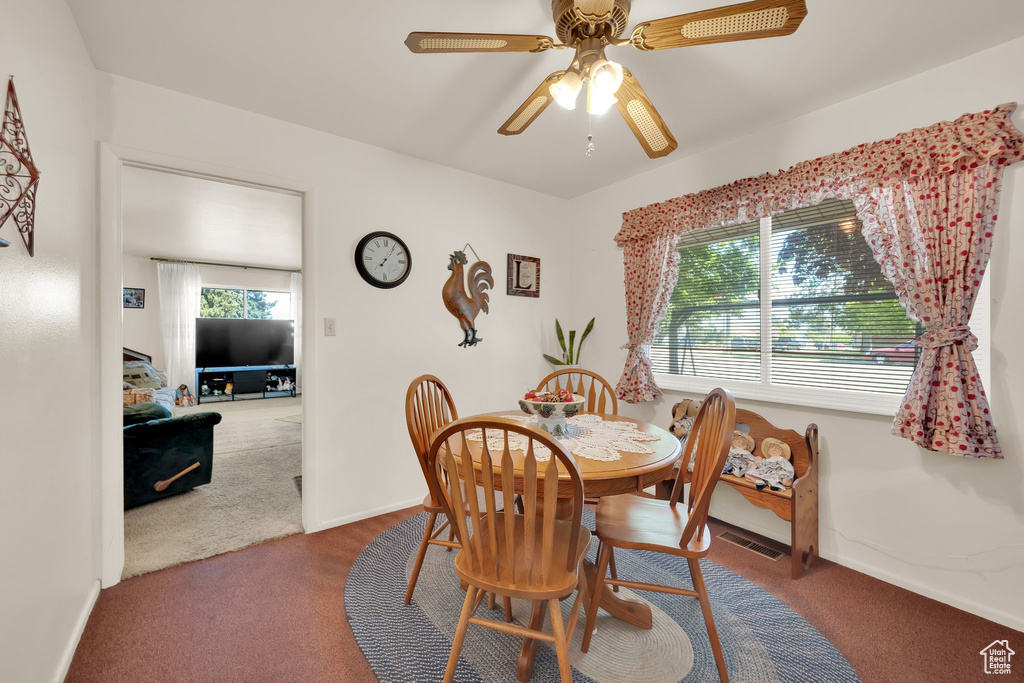Carpeted dining area with ceiling fan and baseboards