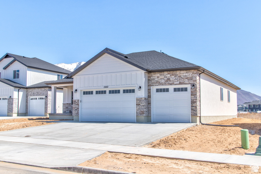 View of front of home with an attached garage, stone siding, concrete driveway, and board and batten siding
