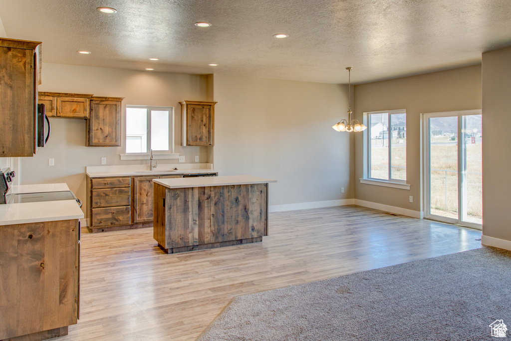 Kitchen featuring brown cabinets, stove, a center island, a textured ceiling, and light wood-style floors