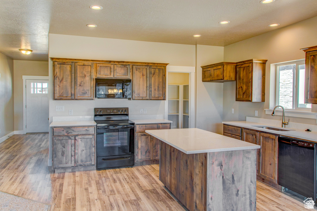 Kitchen with black appliances, a sink, light wood-type flooring, light countertops, and recessed lighting
