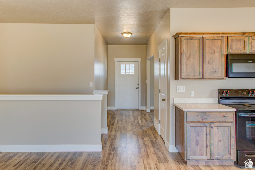 Kitchen with black appliances, light wood-type flooring, light countertops, baseboards, and brown cabinetry
