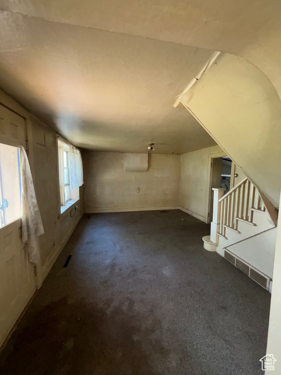 Unfurnished living room featuring stairs and dark colored carpet
