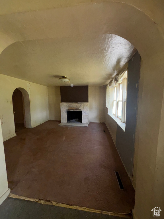 Unfurnished living room featuring a stone fireplace and arched walkways