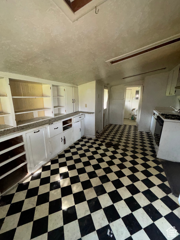 Kitchen with open shelves, light floors, white cabinets, and range with gas stovetop