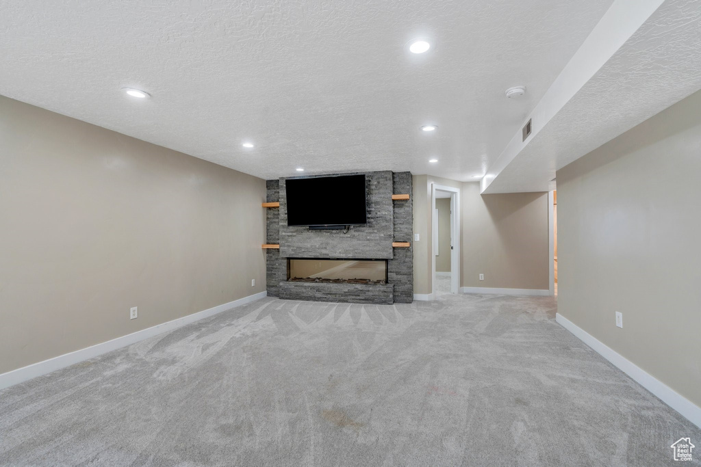 Unfurnished living room with a stone fireplace, carpet floors, a textured ceiling, baseboards, and recessed lighting