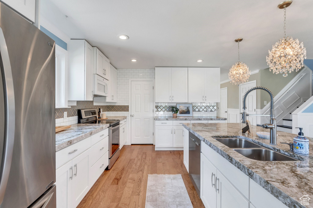 Kitchen with stainless steel appliances, a sink, a chandelier, backsplash, and hanging light fixtures